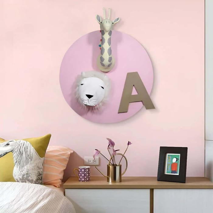 Pink kids bedroom wall featuring a round animal plaque with giraffe and lion heads and letter A above a dresser.