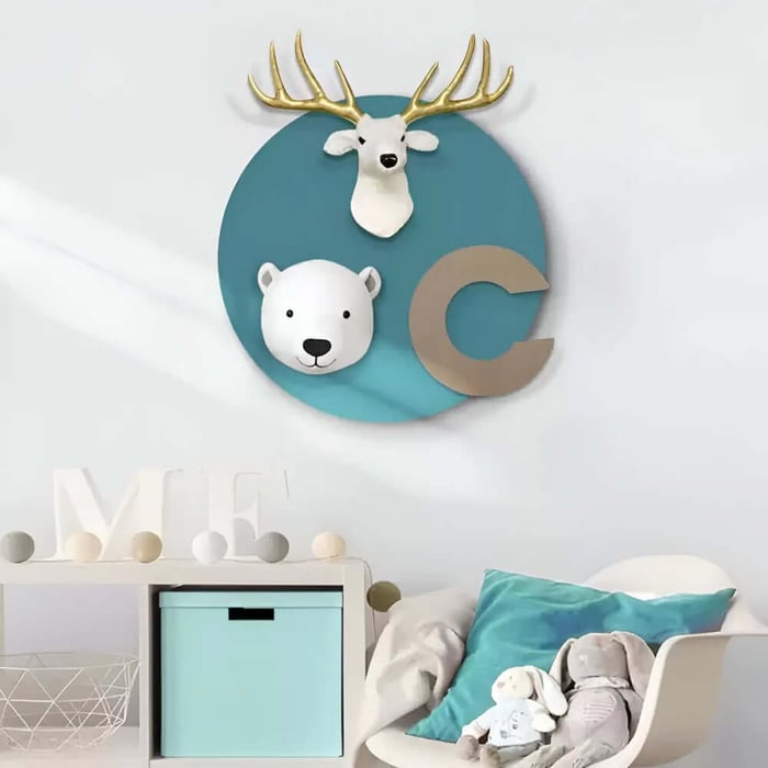 Teal circular kids wall plaque with deer and polar bear heads and letter C above nursery storage unit.