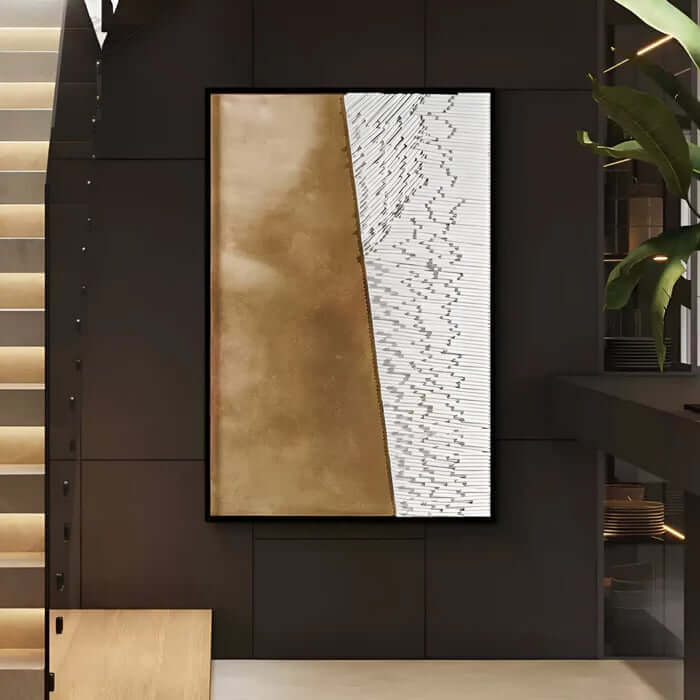 Large abstract wall art with a gold panel and a textured white panel divided by a sharp diagonal, in a modern dark stairwell.