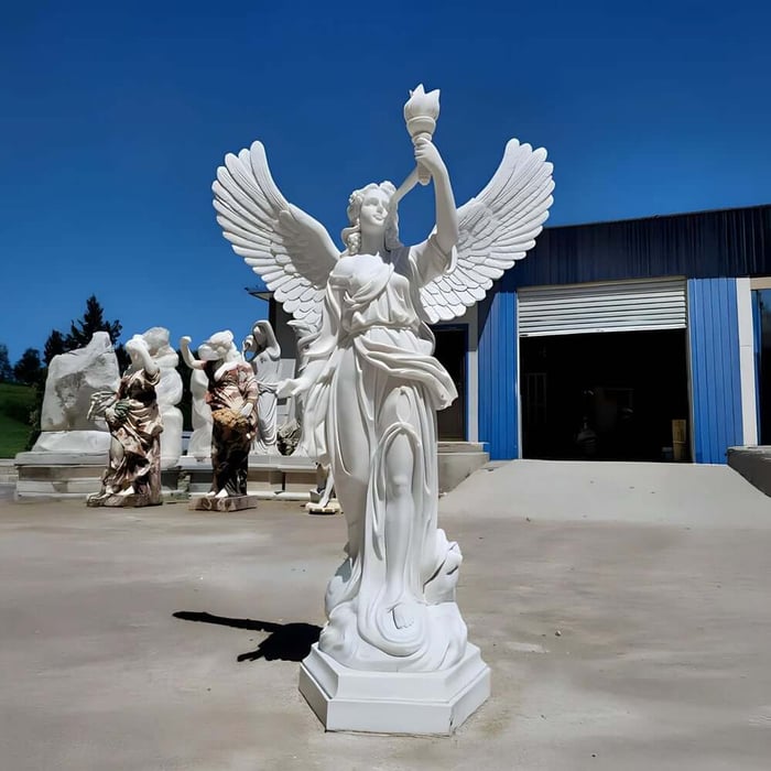 Tall marble angel statue holding a torch aloft outside a sculpture workshop.