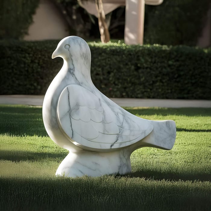 The Pure Grace Dove Marble Outdoor Sculpture by Giant Sculptures, standing at 50cm, rests gracefully on a green lawn. Its simple, smooth curves and etched wing details complement the sunlit garden and trimmed hedges, exuding tranquillity.