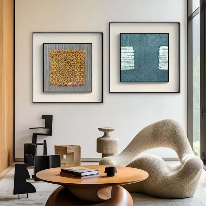 Modern lounge with two framed abstract artworks on a white wall above a sculptural chair and round table.