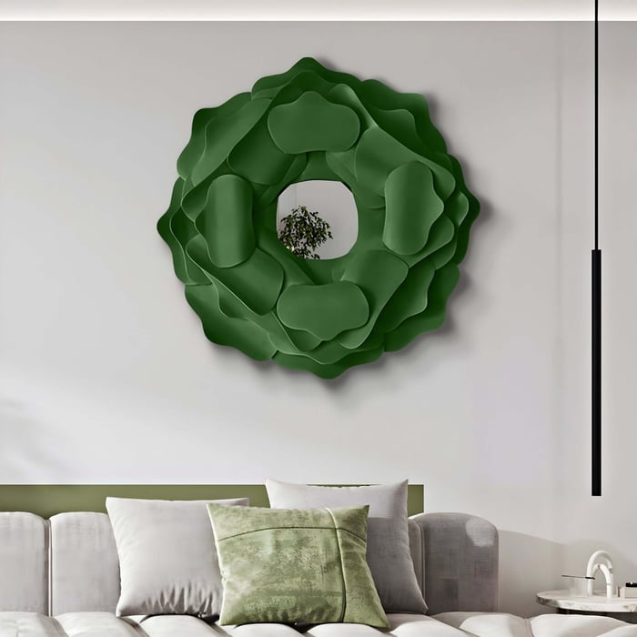 A bedroom features forest green decor with the Sculptura Mirror Forest Green Floral Round Metal Wall Art by Giant Sculptures. Below, a light gray couch is adorned with green and gray pillows, while a slender black pendant light hangs gracefully from the ceiling.