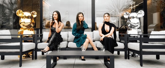 Three women seated outdoors on modern patio furniture, flanked by large gold and silver bear sculptures.