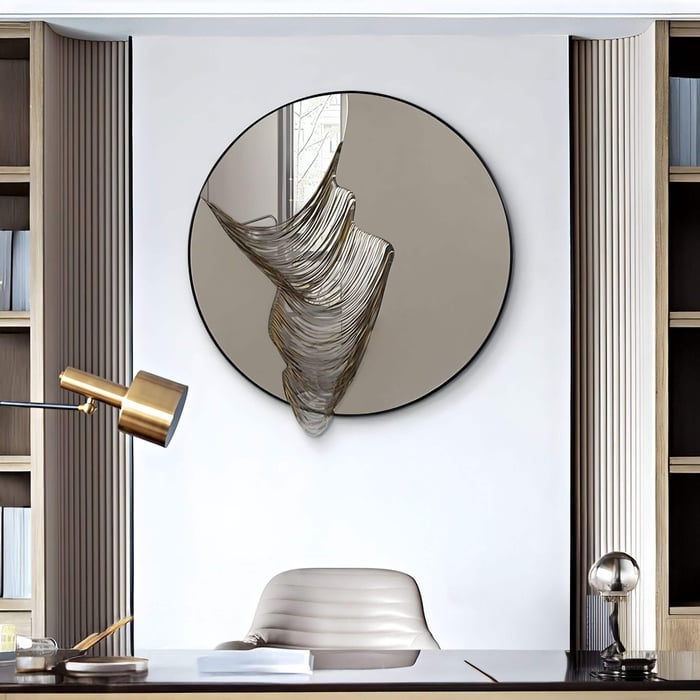 Round mirror with sculptural smoke silver wave detail flowing across the surface, mounted in a modern home office above a desk with brass and neutral-toned accents.