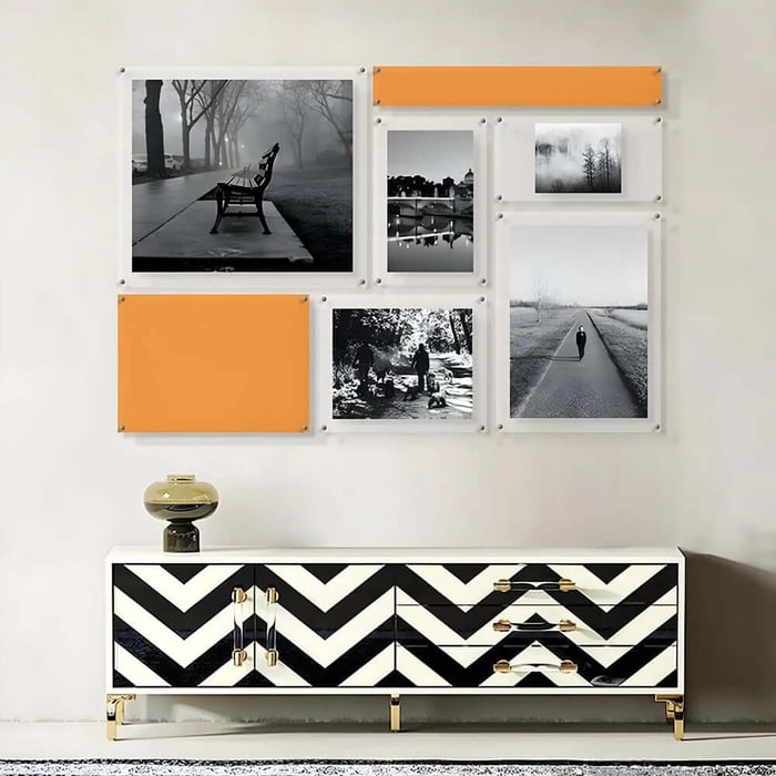 Gallery wall of black-and-white photography prints with orange accent panels above a patterned sideboard.