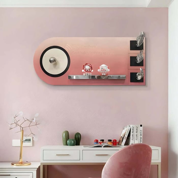 Pink home office wall with a playful mounted art shelf and hooks above a white desk and blush chair.