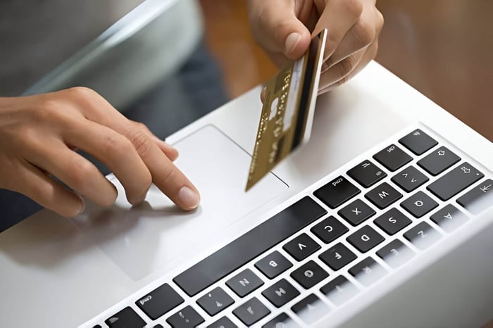 Close-up of a person using a laptop and holding a credit card, illustrating online shopping or digital payment processing.