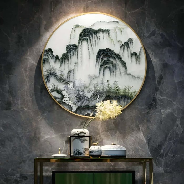 Round framed landscape-style artwork in black and white on a dark marble wall above a console with decorative objects.