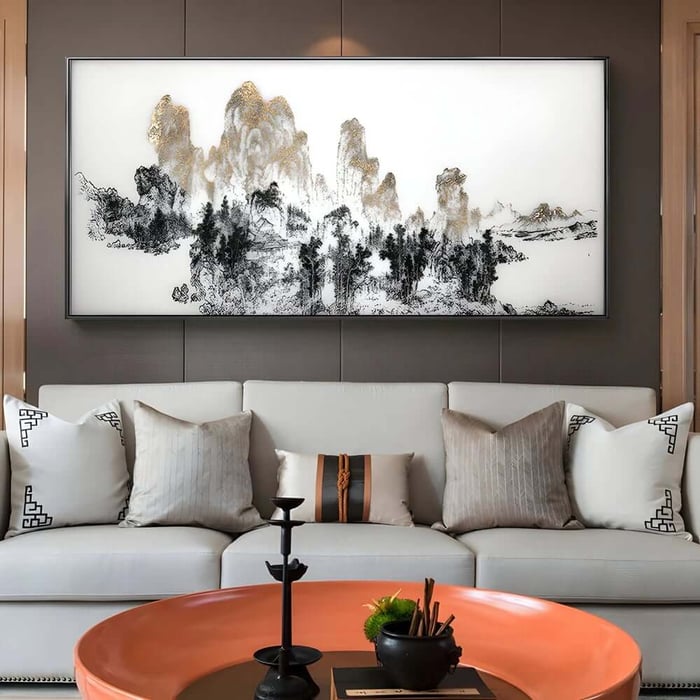 Large panoramic monochrome landscape-style artwork with gold highlights above a white sofa and round orange coffee table.
