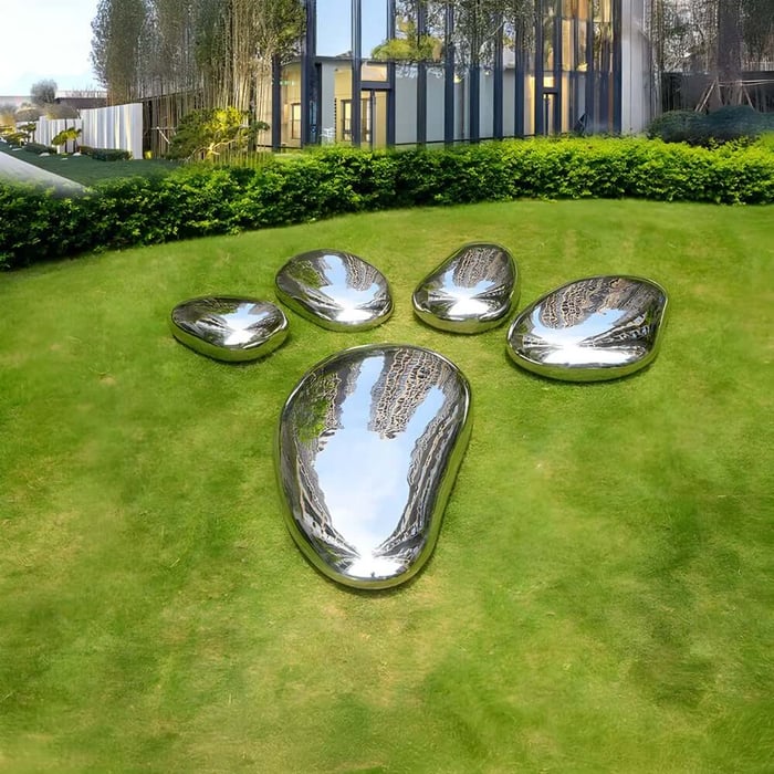 Shiny metallic sculptures arranged on grass in the shape of a large paw print, reflecting the surrounding buildings and sky.