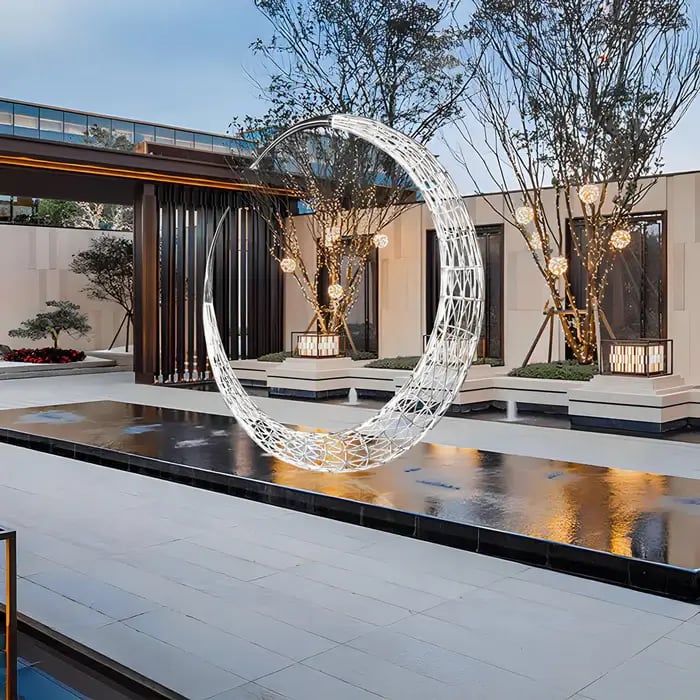 A large, shiny metallic mountain sculpture placed near a water feature in an upscale building's outdoor area.