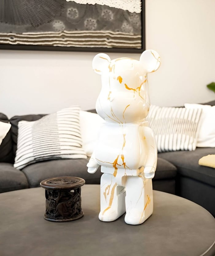 Contemporary golden luster bear sculpture with gold marble detailing displayed on a modern coffee table in a cosy living room setting with a grey sofa and striped cushions.