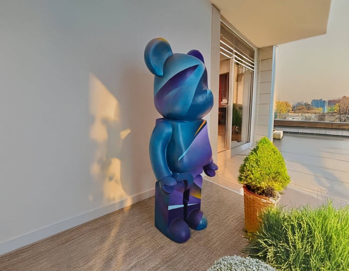 Colorful gradient bear sculpture with abstract shapes, positioned on a balcony garden with a view of the city skyline.