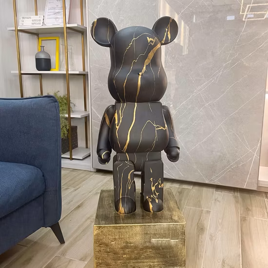 Abstract silver resin bear sculpture with gold ears and hands displayed on a black pedestal in a stylish modern living room.