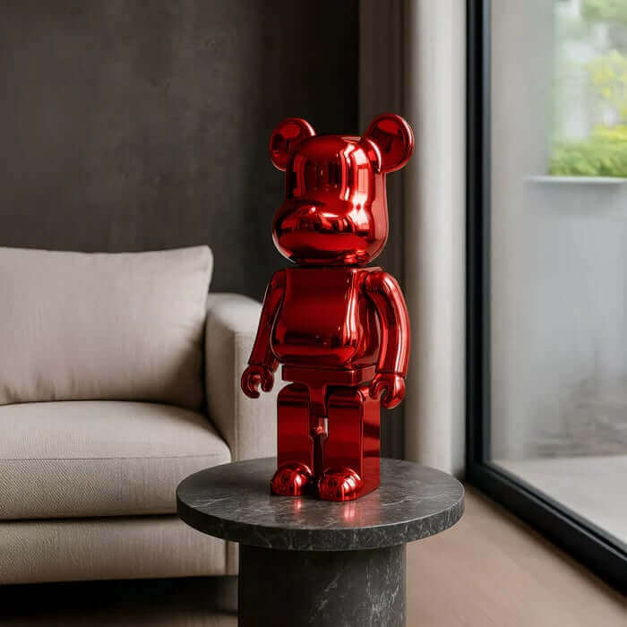 A glossy red bear-shaped resin sculpture displayed on a round black marble side table beside a beige sofa in a modern living room.