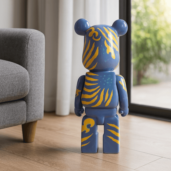 Blue bear-shaped resin sculpture with yellow patterns standing on a wooden floor beside a grey sofa and large window in a modern living room.
