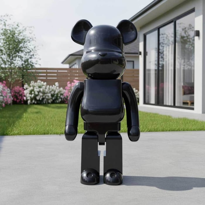 Glossy black bear-shaped resin sculpture standing outdoors on a driveway in front of a modern home and garden.