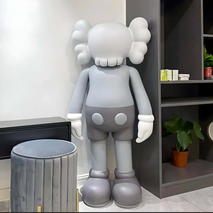 Large grey and white resin sculpture figure standing in a corner beside shelving in a contemporary room.