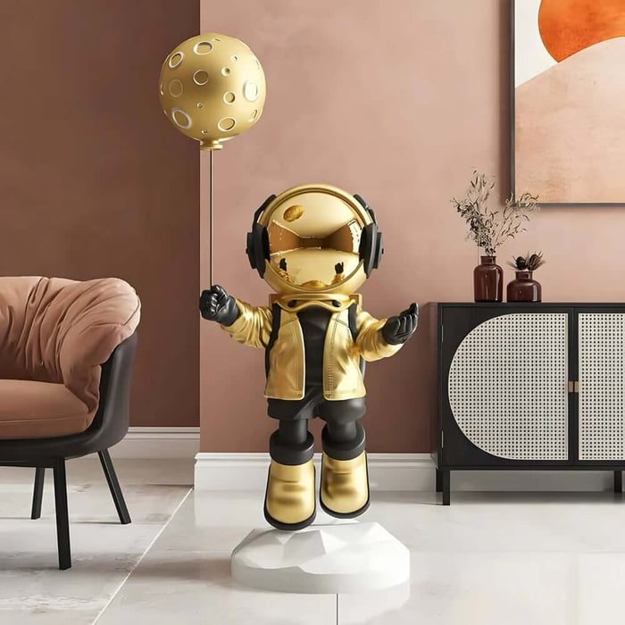 Gold astronaut resin sculpture holding a moon balloon, displayed indoors as a statement décor piece.