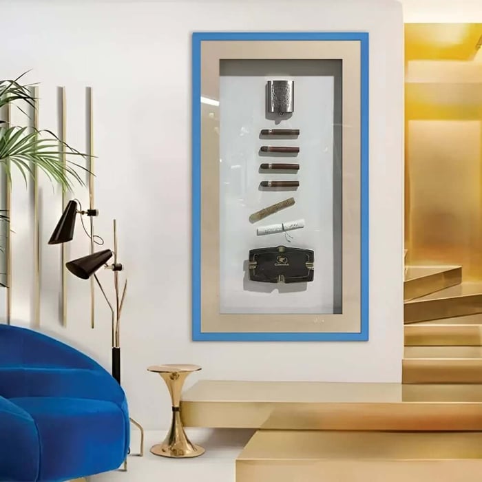 Tall framed shadowbox with cigars and cigar accessories displayed in a bright modern interior.