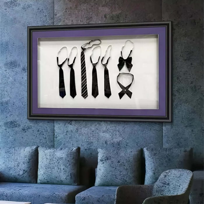 Framed display of black neckties and a bow tie arranged in a row on a textured blue wall above a sofa.