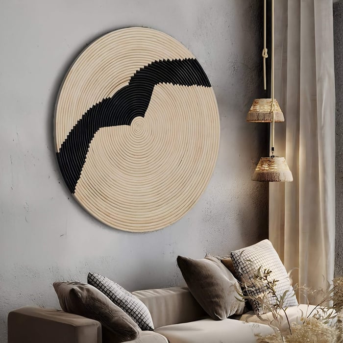 A modern living room features neutral cushions, textured beige walls, woven pendant lights, and the Giant Sculptures Artura Ivory Round Hand-Painted 3D Relief Wall Art with concentric patterns and a bold black zigzag.