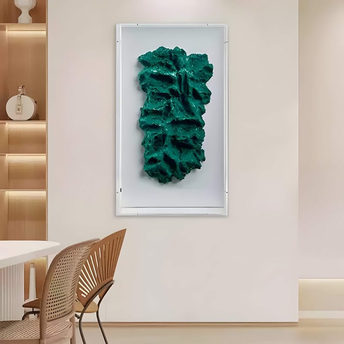 Contemporary 3D wall art featuring an emerald green sandstone relief with rugged, organic textures, framed in white, displayed in a modern dining space.