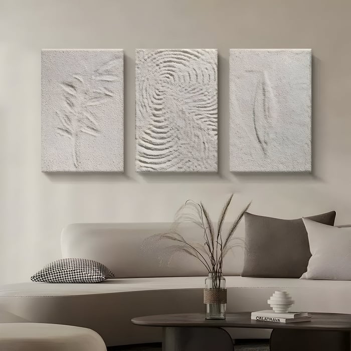 Minimalist beige triptych wall art featuring organic embossed textures resembling a leaf, ripples, and abstract forms, displayed above a modern curved sofa with neutral decor.