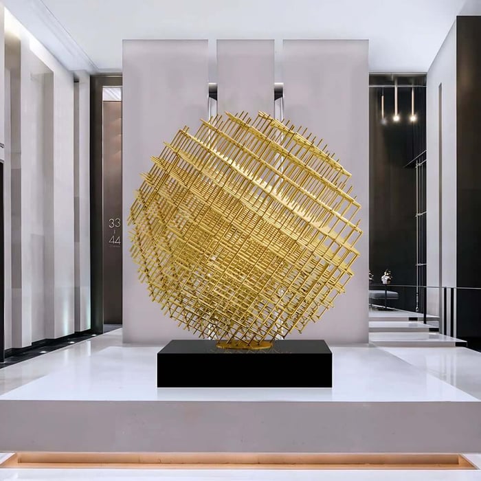 Large gold lattice sphere geometric sculpture centred on a plinth in a modern lobby.