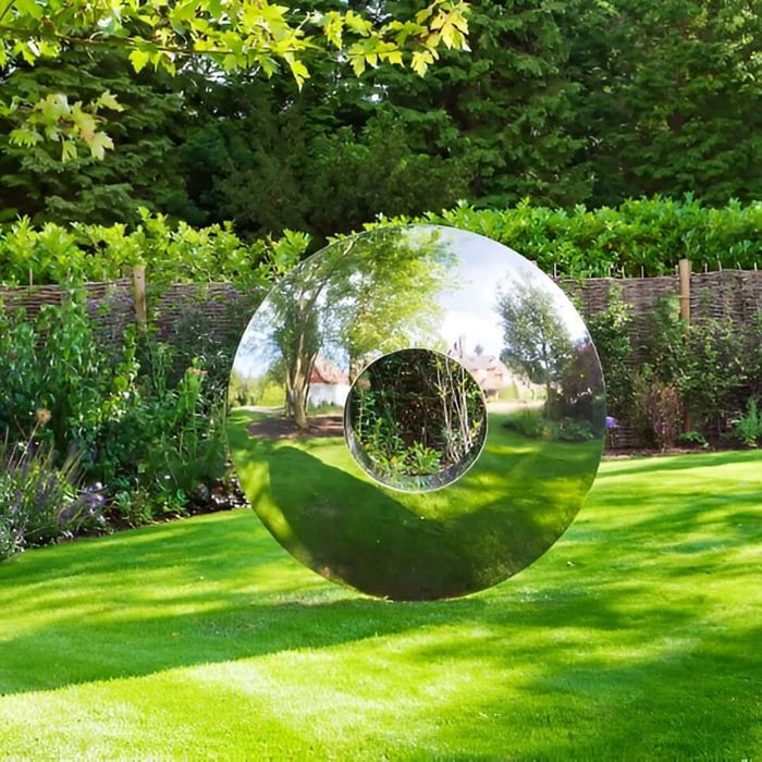Polished stainless steel Torus sculpture by David Harber displayed in a landscaped garden, reflecting trees, lawn, and surrounding greenery.