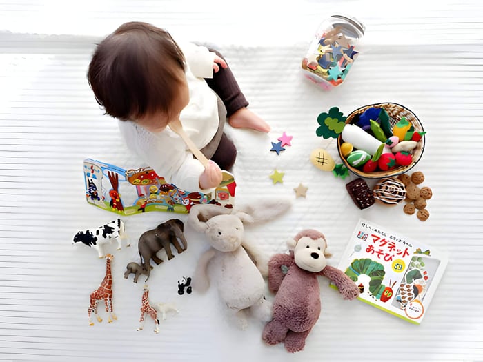 a toddler on a cream blanket surrounded by toys