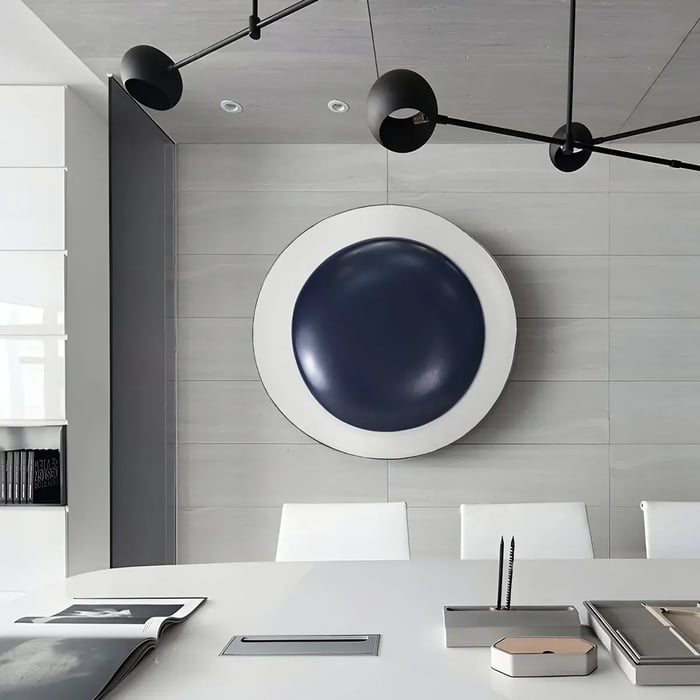  A modern office with a large, circular wall sculpture featuring a navy domed center on a white background, creating a striking contrast in the neutral-toned space.