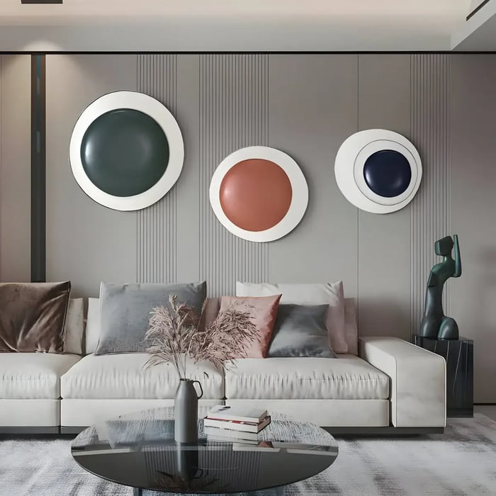 A sophisticated living area showcasing three circular wall sculptures with glossy, domed centers in dark green, burnt orange, and deep navy, set against a textured gray panel wall.