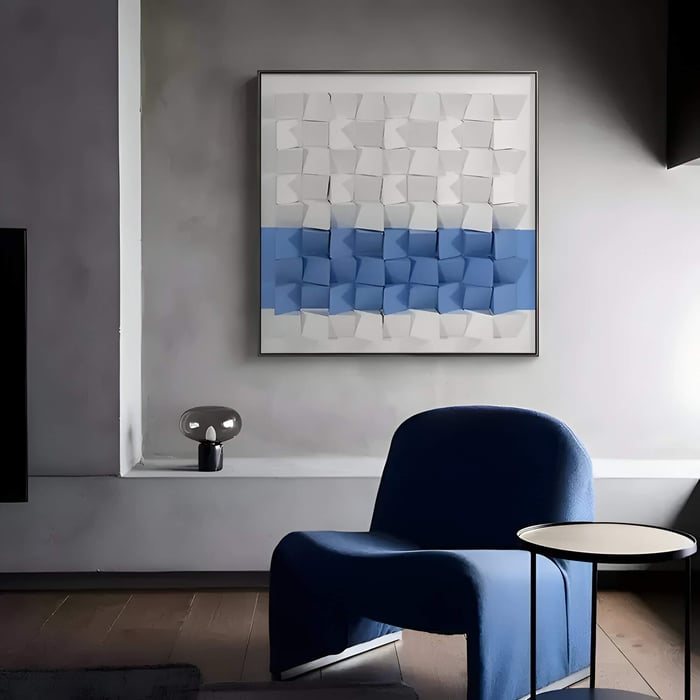 Modern minimalist living room with a blue lounge chair, small round side table, and large abstract 3D Nordic wall art in white and blue on a grey wall.