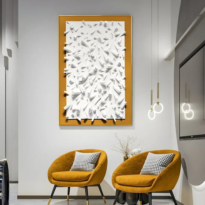 A white, sculptural wall art piece framed with a yellow border, featuring dynamic shapes and textures, set in a modern living room with mustard-colored chairs and minimalistic lighting.