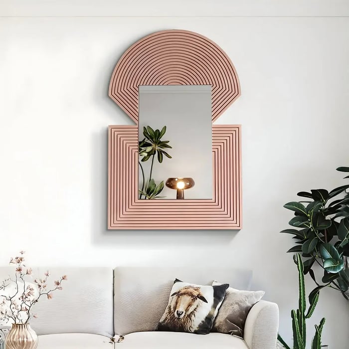  A uniquely designed pink geometric mirror placed above a plush sofa, reflecting a warm-lit lamp and decorative greenery.