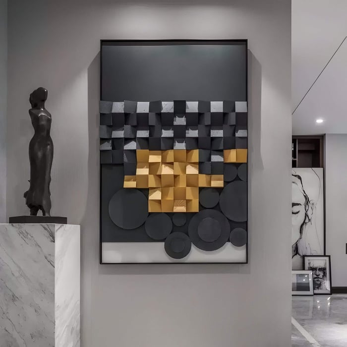 Modern 3D geometric wooden wall art featuring layered black, grey, and gold elements, displayed in an elegant interior alongside a marble pedestal with a bronze sculpture.