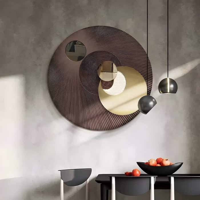 Modern round abstract wall mirror art above a black dining table with pendant lights and fruits.