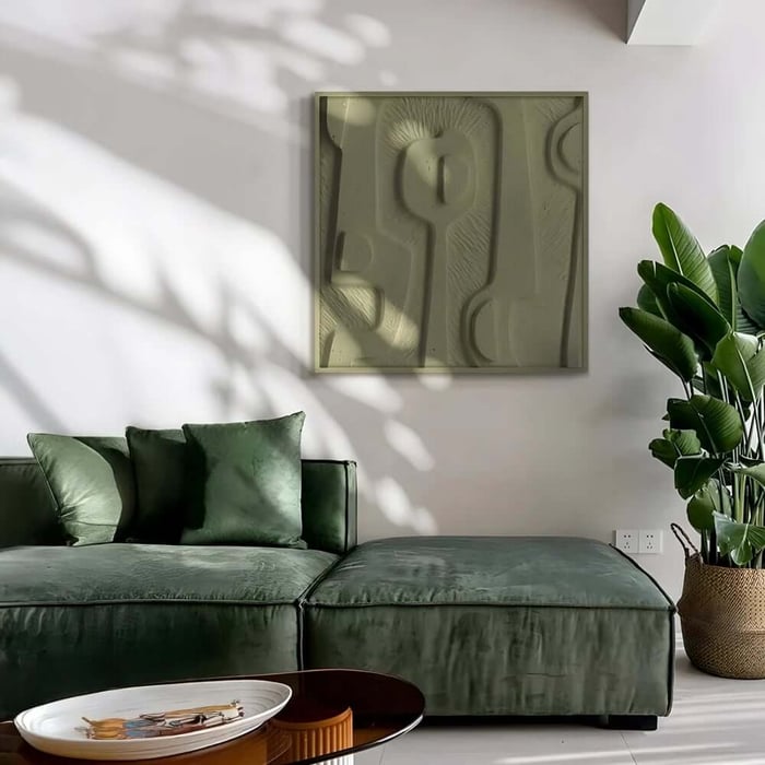 Olive-green textured abstract artwork above a green velvet sofa, with soft sunlight and a large indoor plant.