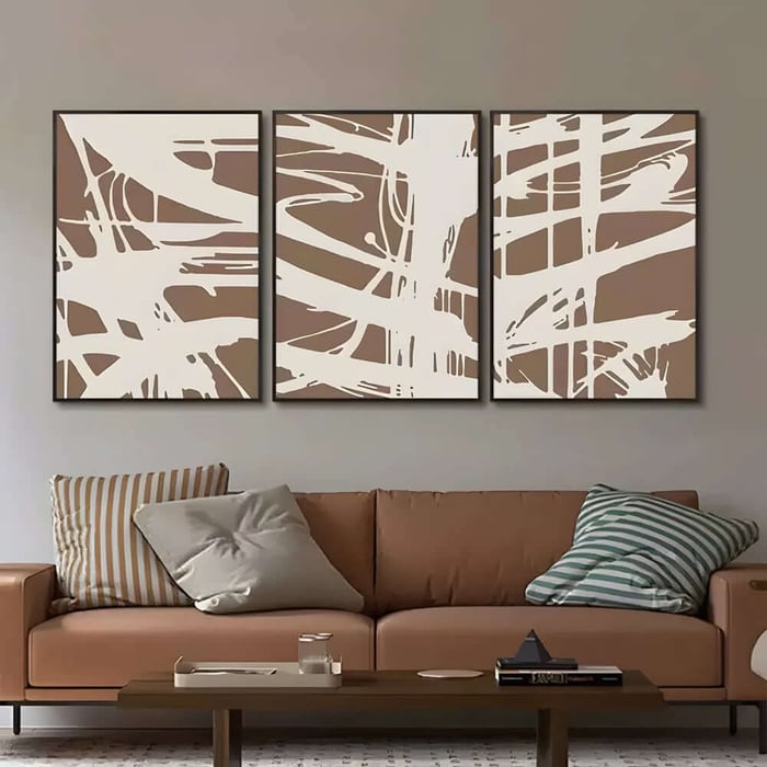 Three-panel abstract print set in beige and white above a tan sofa in a modern living room.