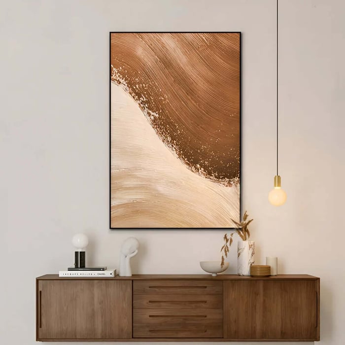 Warm beige and brown abstract canvas above a wooden sideboard with soft lighting and simple styling.