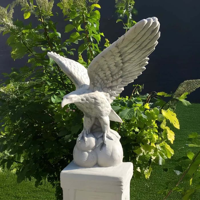 White marble eagle wildlife sculpture with wings spread on pedestal in garden setting.