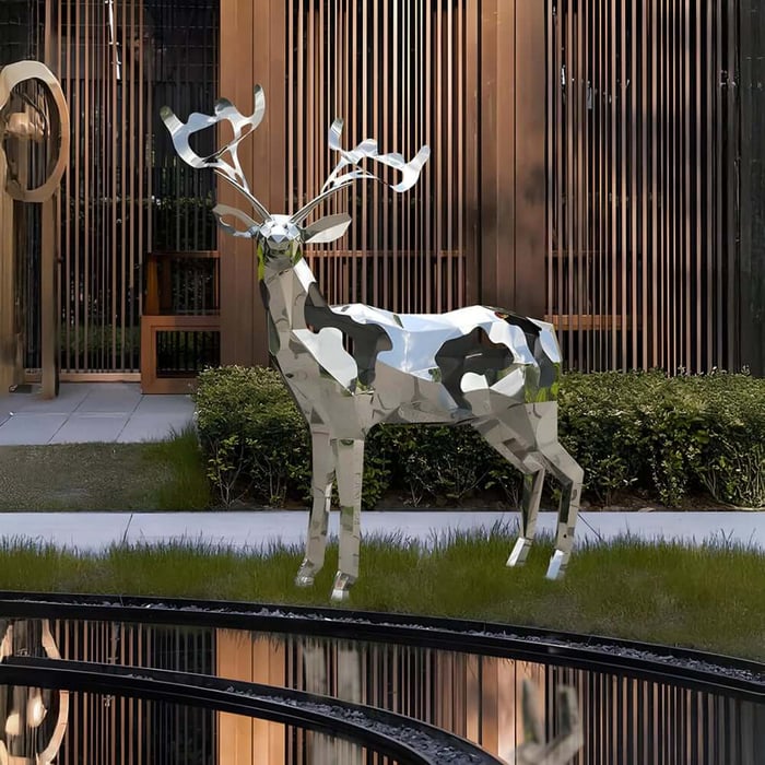 Polished stainless-steel deer sculpture with faceted surfaces, standing on a lawn beside a reflective pool in a modern courtyard with slatted walls.
