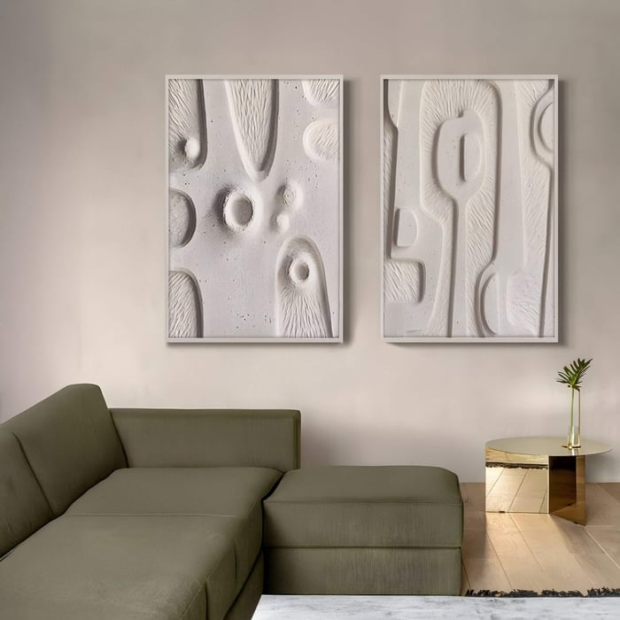 Wabi sabi art in textured ivory tones displayed above a green sectional, embracing imperfection through raw minimalist forms.