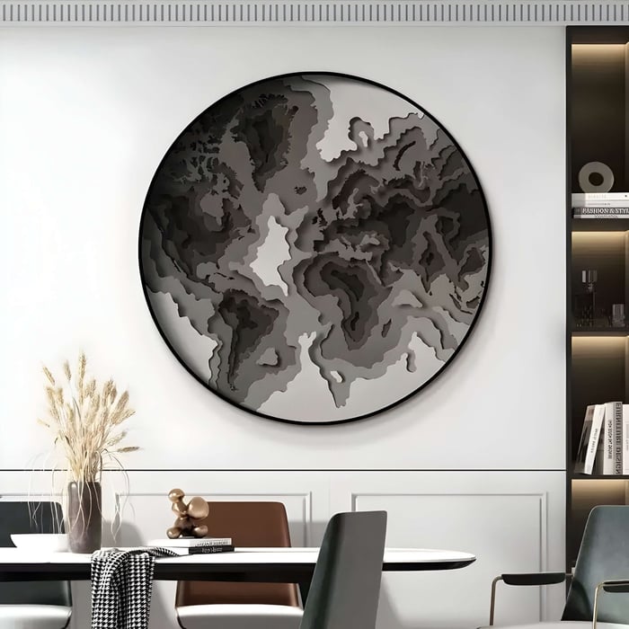 Large round topographic-style wall piece in grayscale tones above a contemporary table and shelving unit.