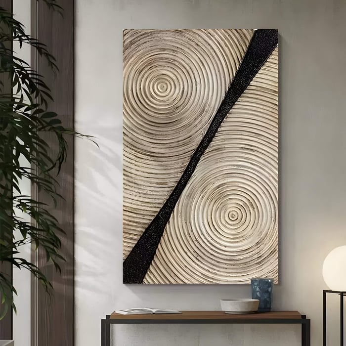 The Artura Ivory Hand-Painted 3D Relief Wall Art by Giant Sculptures features beige concentric circles and a bold black stripe, adding minimalist tranquillity above a console with a bowl, blue vase, plant, and round lamp.