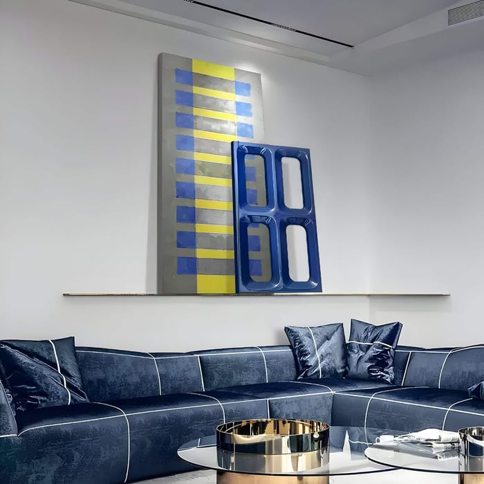 Geometric abstract 3D art in yellow, blue, and grey tones enhances the look of a sleek navy velvet sectional couch area.
