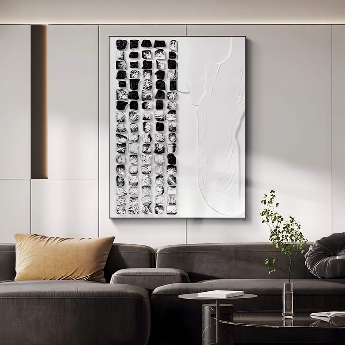 In a modern living room, the Aestilis Black & White Mosaic Wood Carving 3D Wall Art by Giant Sculptures adorns a white paneled wall. A dark gray sofa with a beige pillow enhances the chic look, while a small plant adds natural charm.