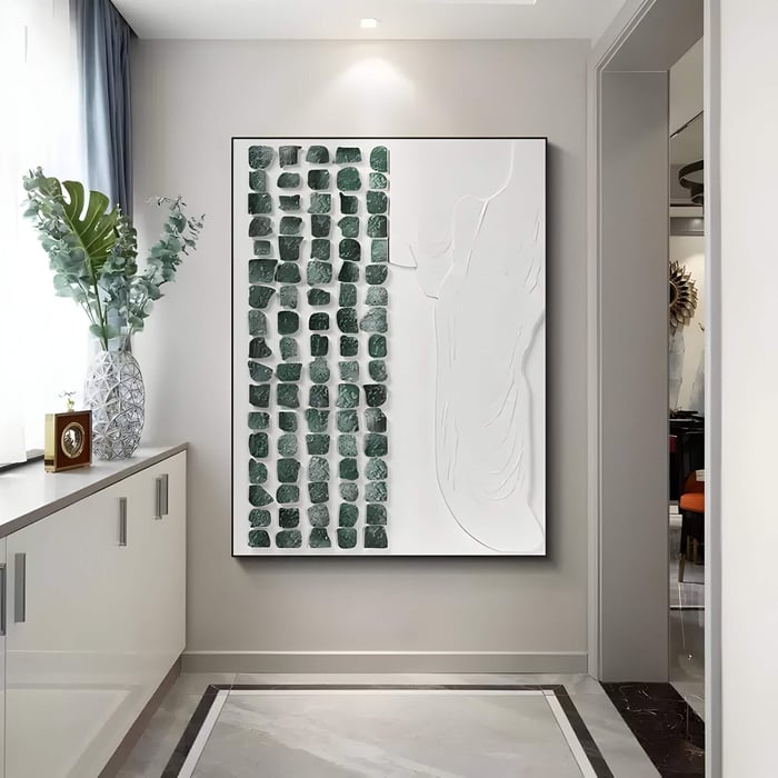 A modern interior features the Aestilis Green & White Mosaic Wood Carving 3D Wall Art by Giant Sculptures with a green stone grid on the left and white design on the right, a vase with greenery on a cabinet beneath a window, and visually interesting hand-carved wood flooring.
